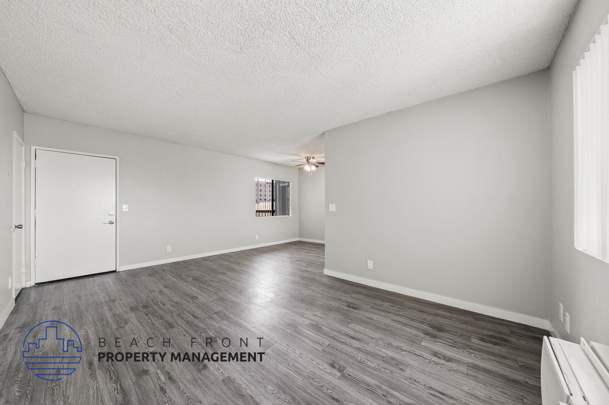 A spacious room with wooden flooring and a logo for Beach Front Property Management in the corner.